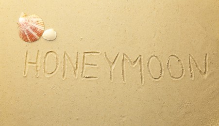 Word Honeymoon written on sand and seashells, top view