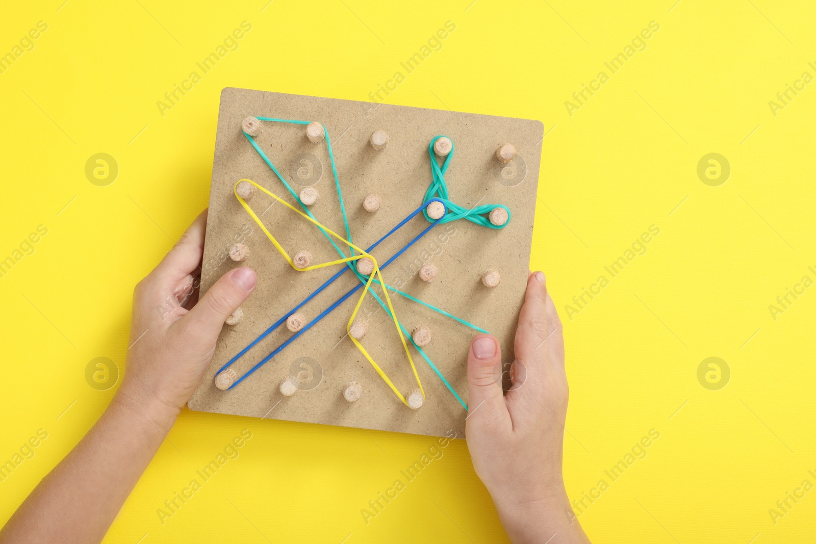 Photo of Motor skills development. Boy with geoboard and rubber bands at yellow table, top view