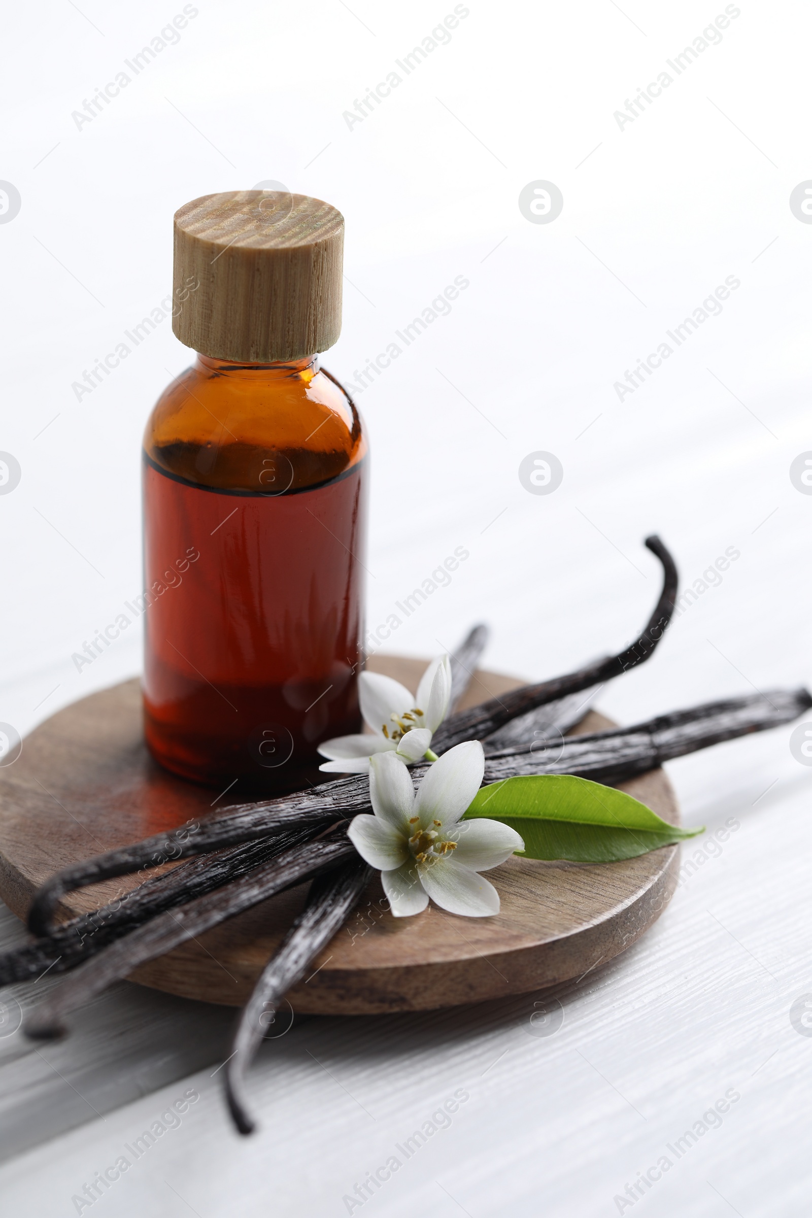 Photo of Vanilla pods, flowers, leaf and bottle with essential oil on white wooden table, closeup