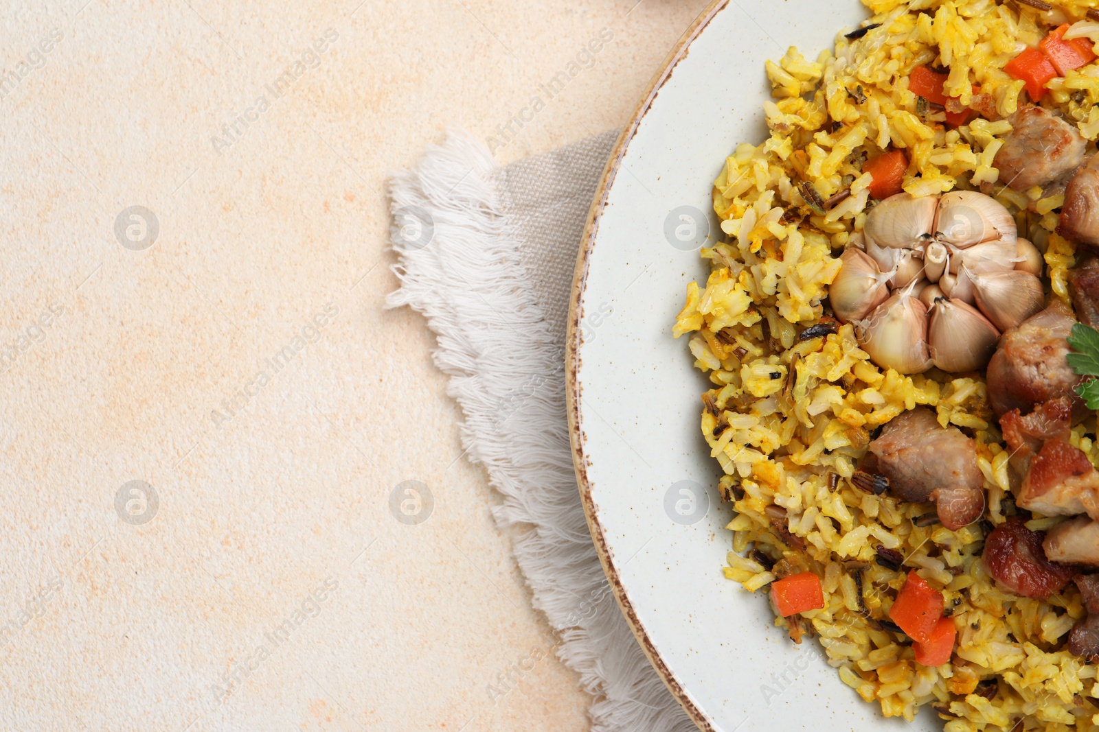 Photo of Delicious pilaf with meat, carrot and garlic on beige table, top view. Space for text