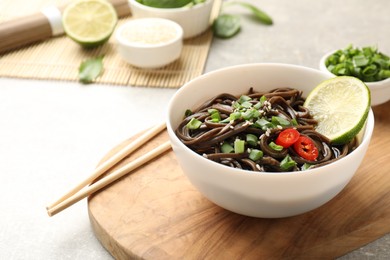 Photo of Tasty buckwheat noodles (soba) with sauce, onion in bowl and chopsticks on table. Space for text