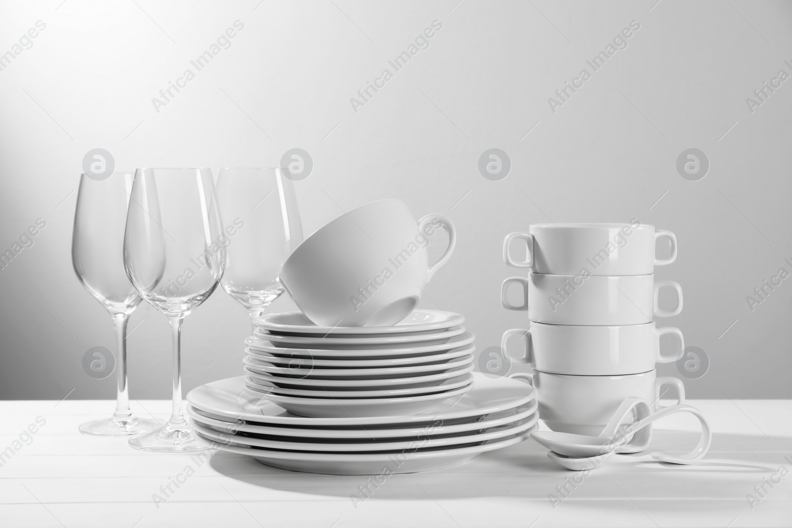 Photo of Set of clean dishware and glasses on white wooden table against light background