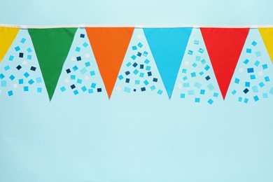 Photo of Bunting with colorful triangular flags and confetti on light blue background, flat lay. Space for text