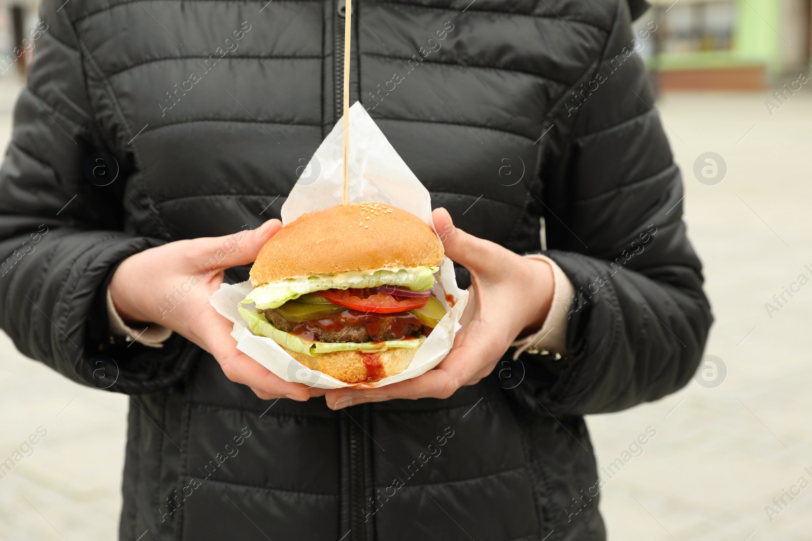 Photo of Woman holding fresh delicious burger outdoors, closeup. Street food