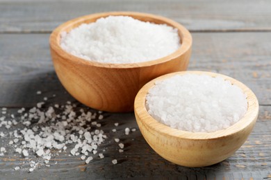 Photo of Bowls of natural sea salt on grey wooden table, closeup