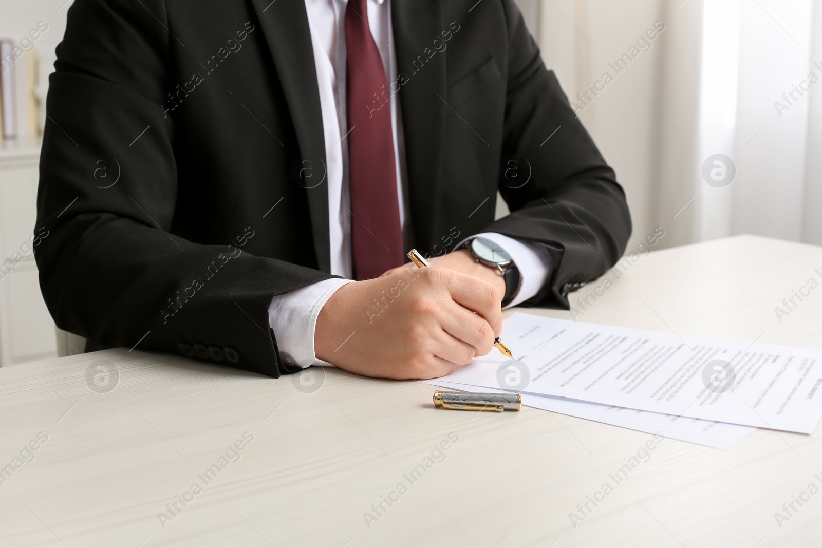 Photo of Notary signing document at wooden table indoors, closeup