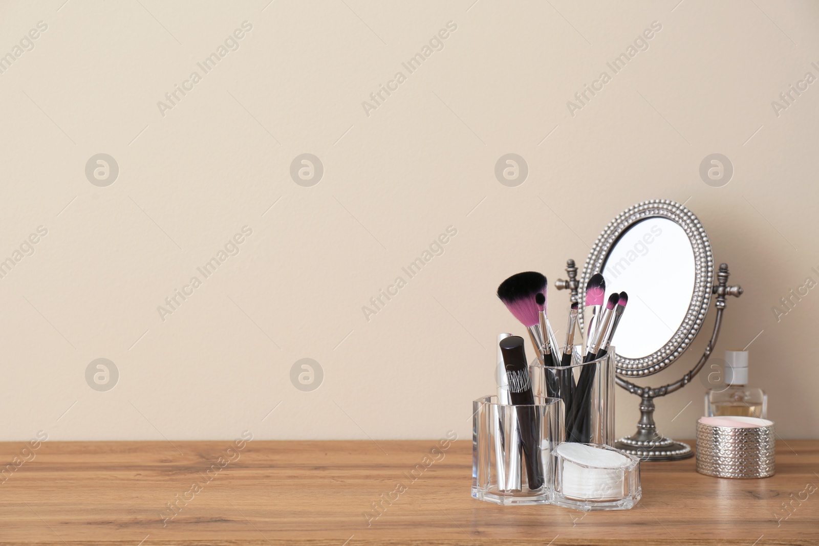 Photo of Organizer with makeup cosmetic products and mirror on table against light wall. Space for text