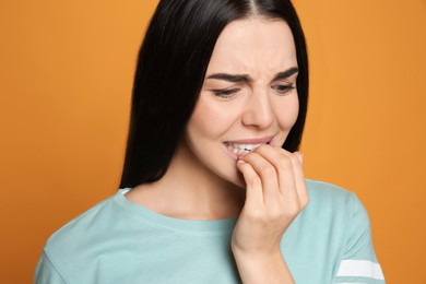 Photo of Young woman biting her nails on yellow background