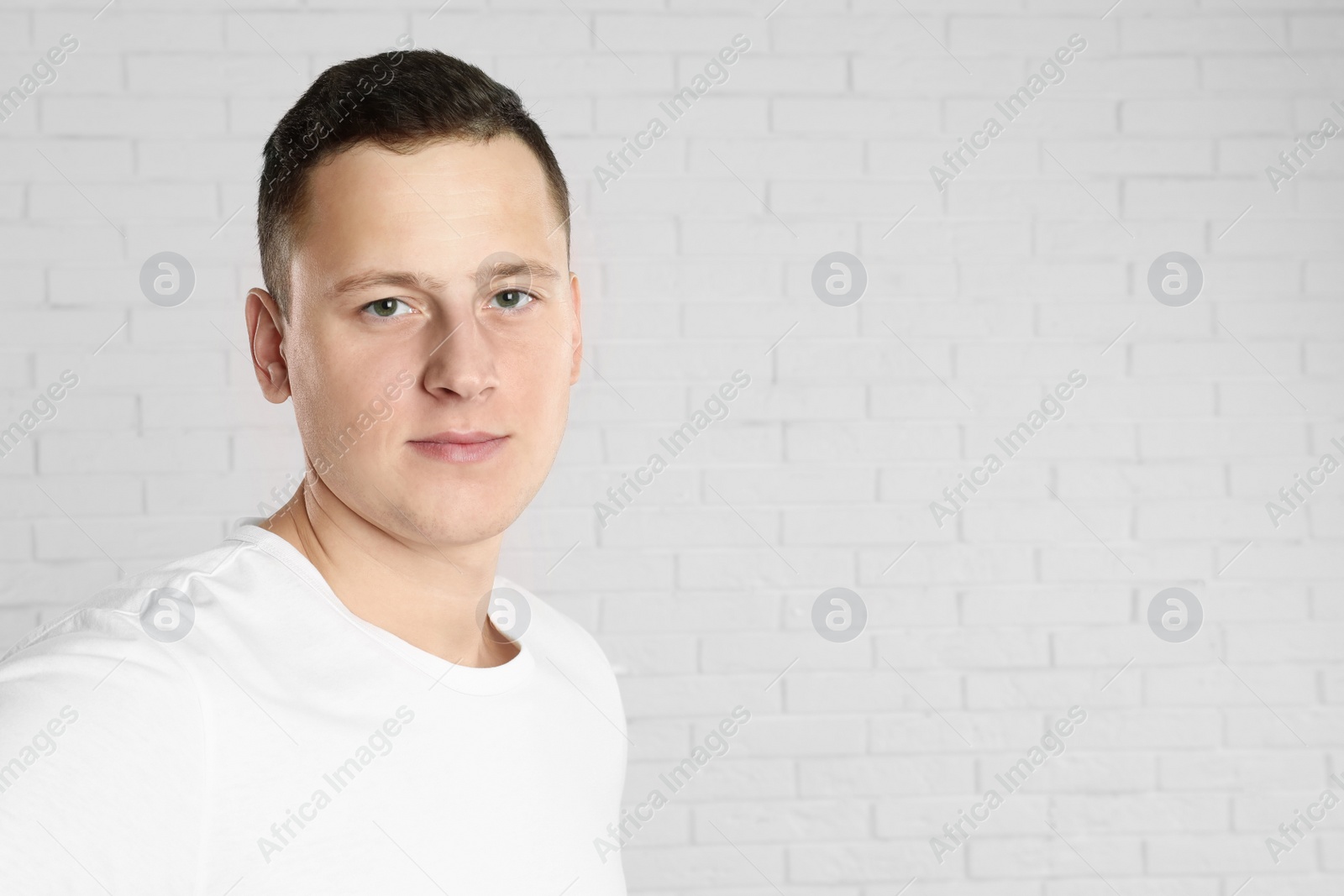 Photo of Handsome young man near white brick wall. Space for text