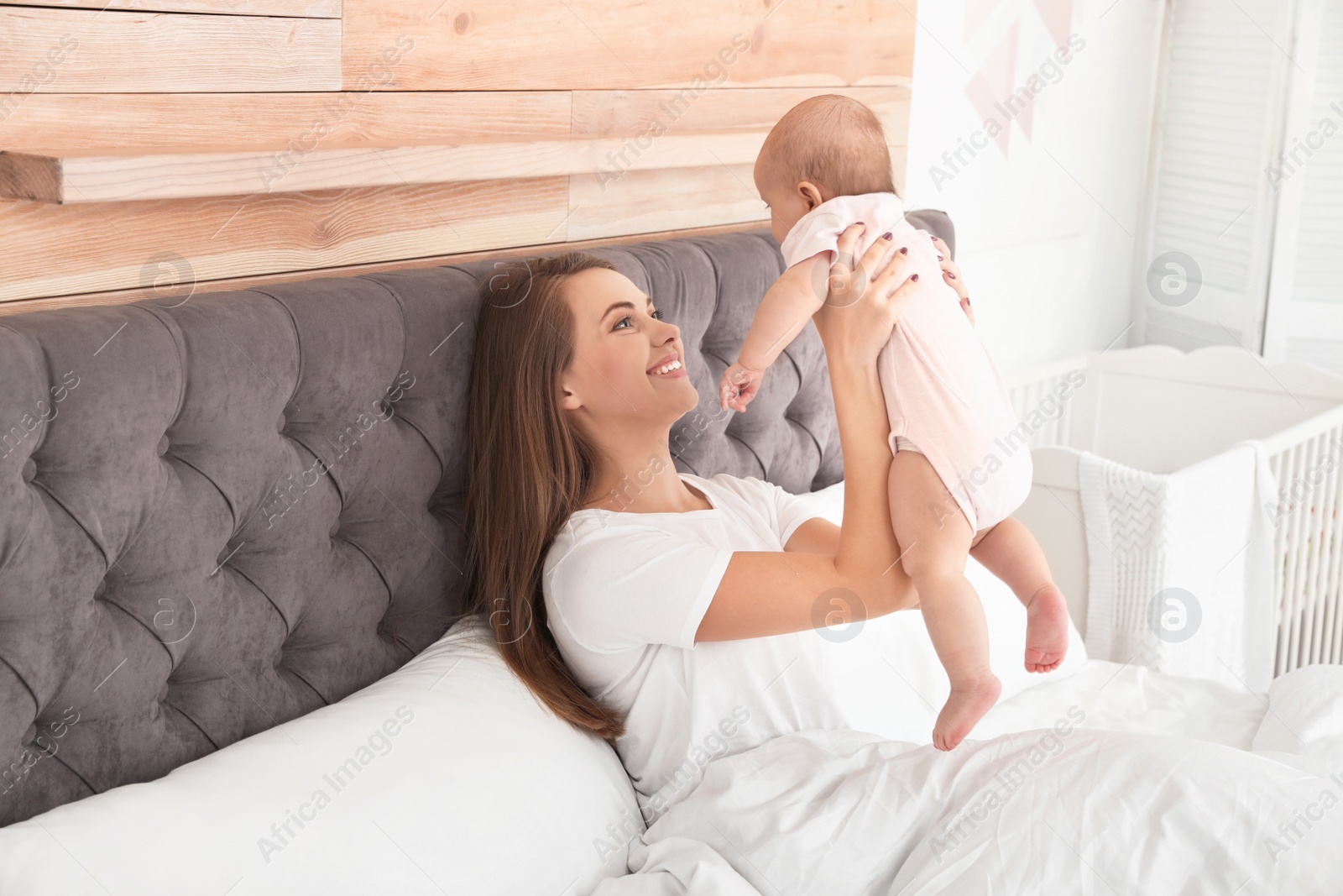 Photo of Young mother playing with her cute baby on bed indoors