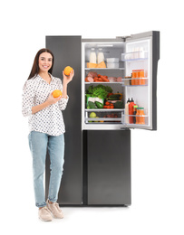 Young woman with oranges near open refrigerator on white background