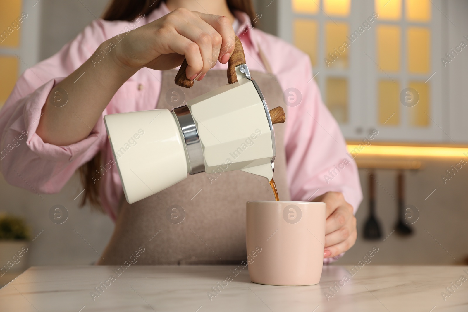 Photo of Woman pouring aromatic coffee from moka pot into cup at white marble table, closeup