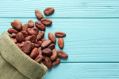 Cocoa beans in bag on blue wooden table, top view. Space for text