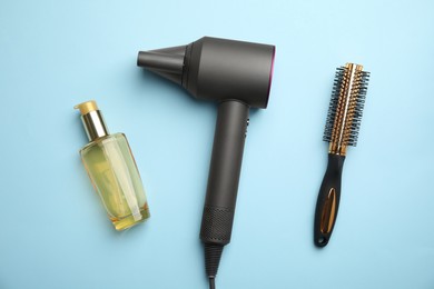 Hair care product, dryer and round brush on light blue background, flat lay