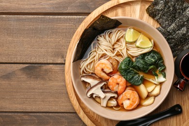 Photo of Delicious ramen with shrimps and mushrooms in bowl served on wooden table, top view with space for text. Noodle soup