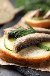 Delicious sandwich with sprats, cucumbers and dill on slate board, closeup