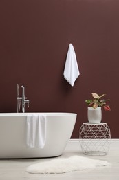 Modern ceramic bathtub and plant near burgundy wall indoors