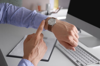 Young man checking time on his wristwatch at workplace