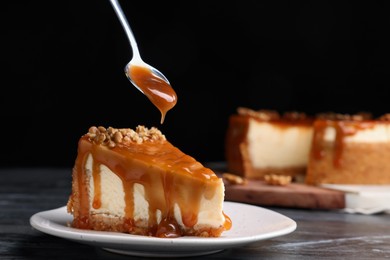 Pouring caramel sauce onto delicious piece of cheesecake with walnuts on black marble table, space for text
