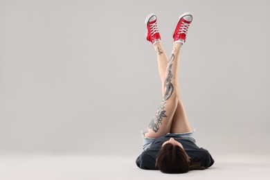 Woman with beautiful tattoos lying on grey background. Space for text