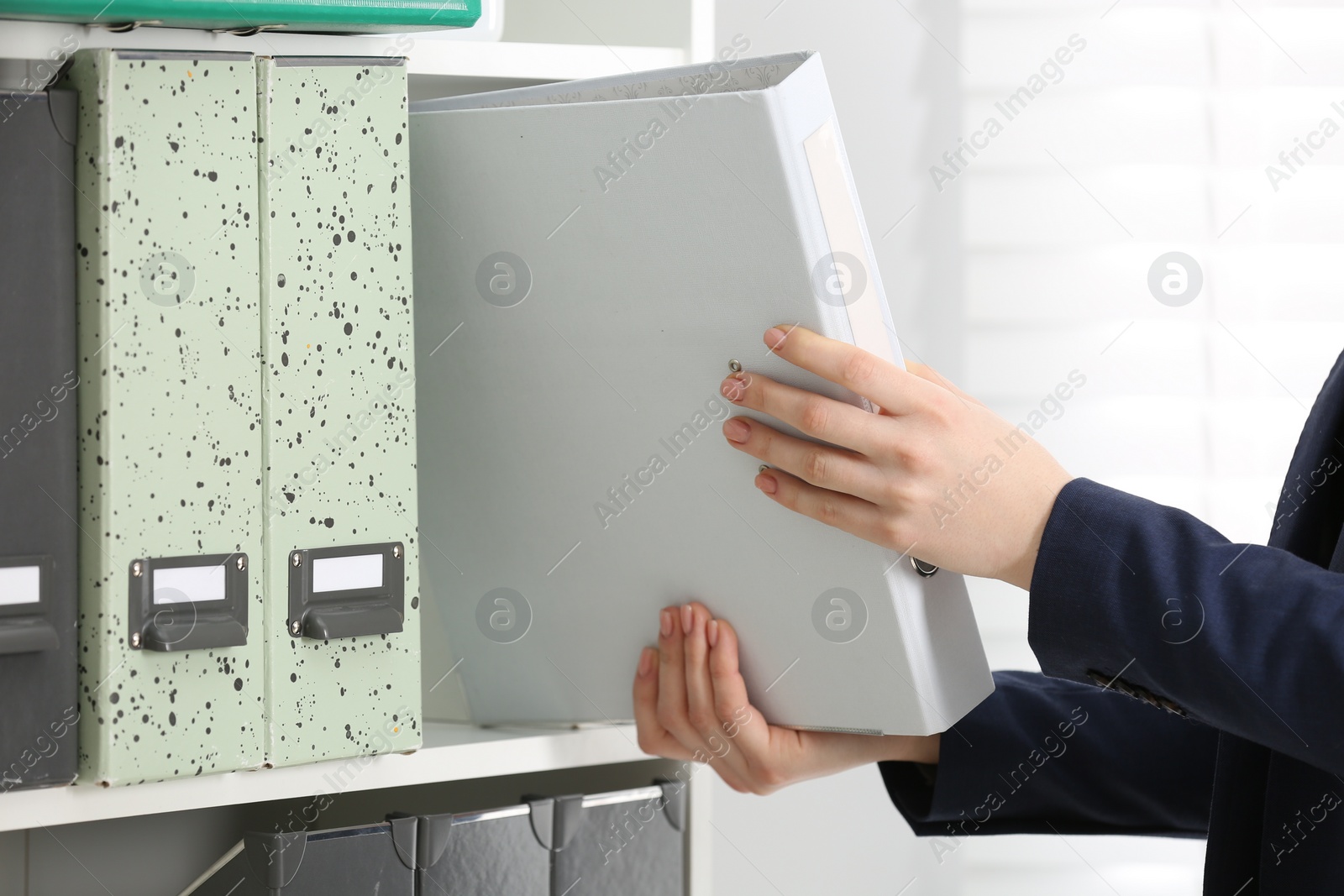 Photo of Woman taking folder with documents from shelf in office, closeup