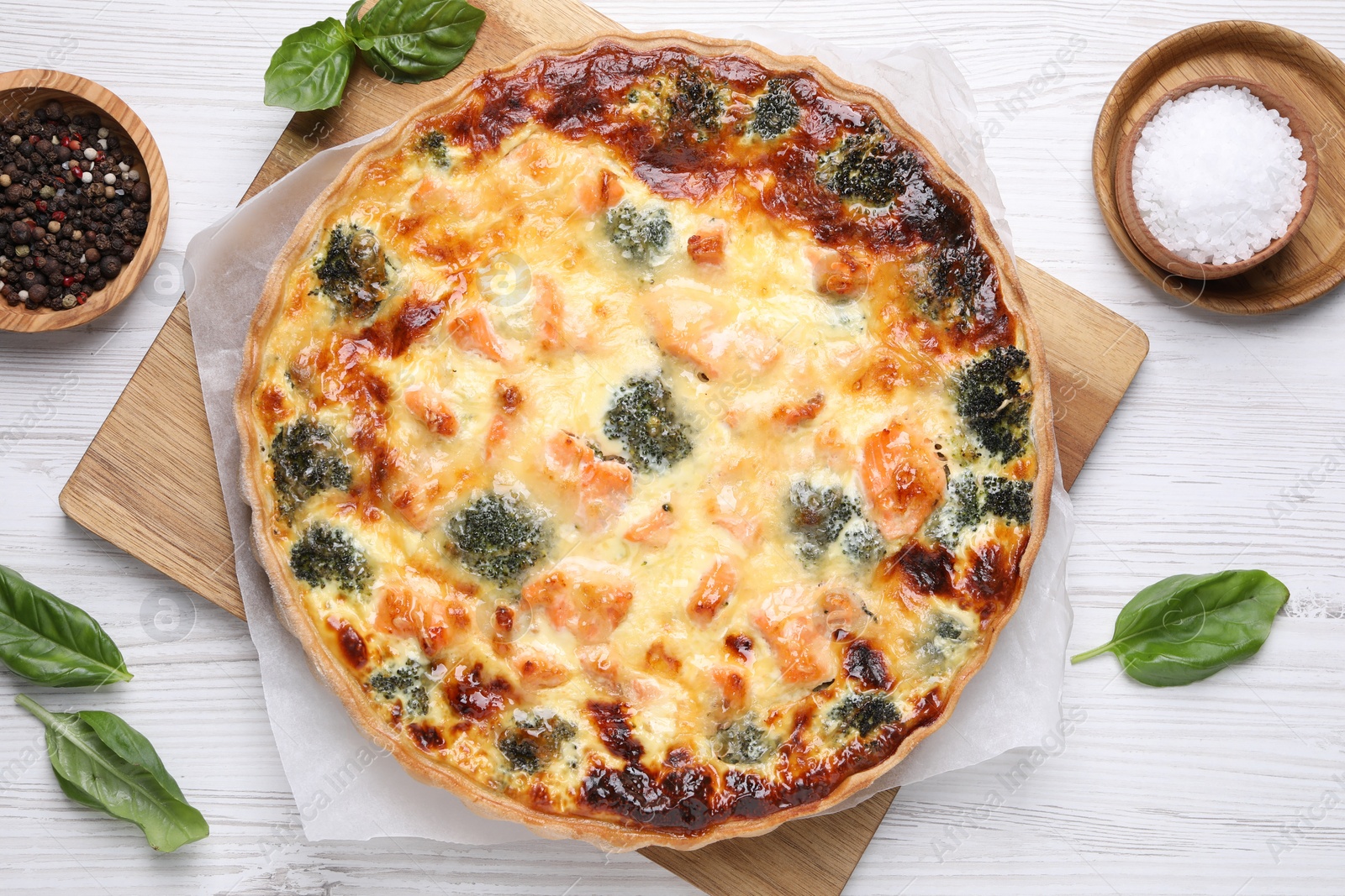 Photo of Delicious homemade quiche with salmon, broccoli, basil leaves and spices on wooden table, flat lay