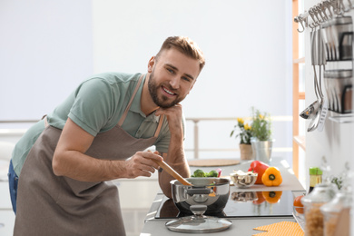 Photo of Young man cooking delicious soup in kitchen