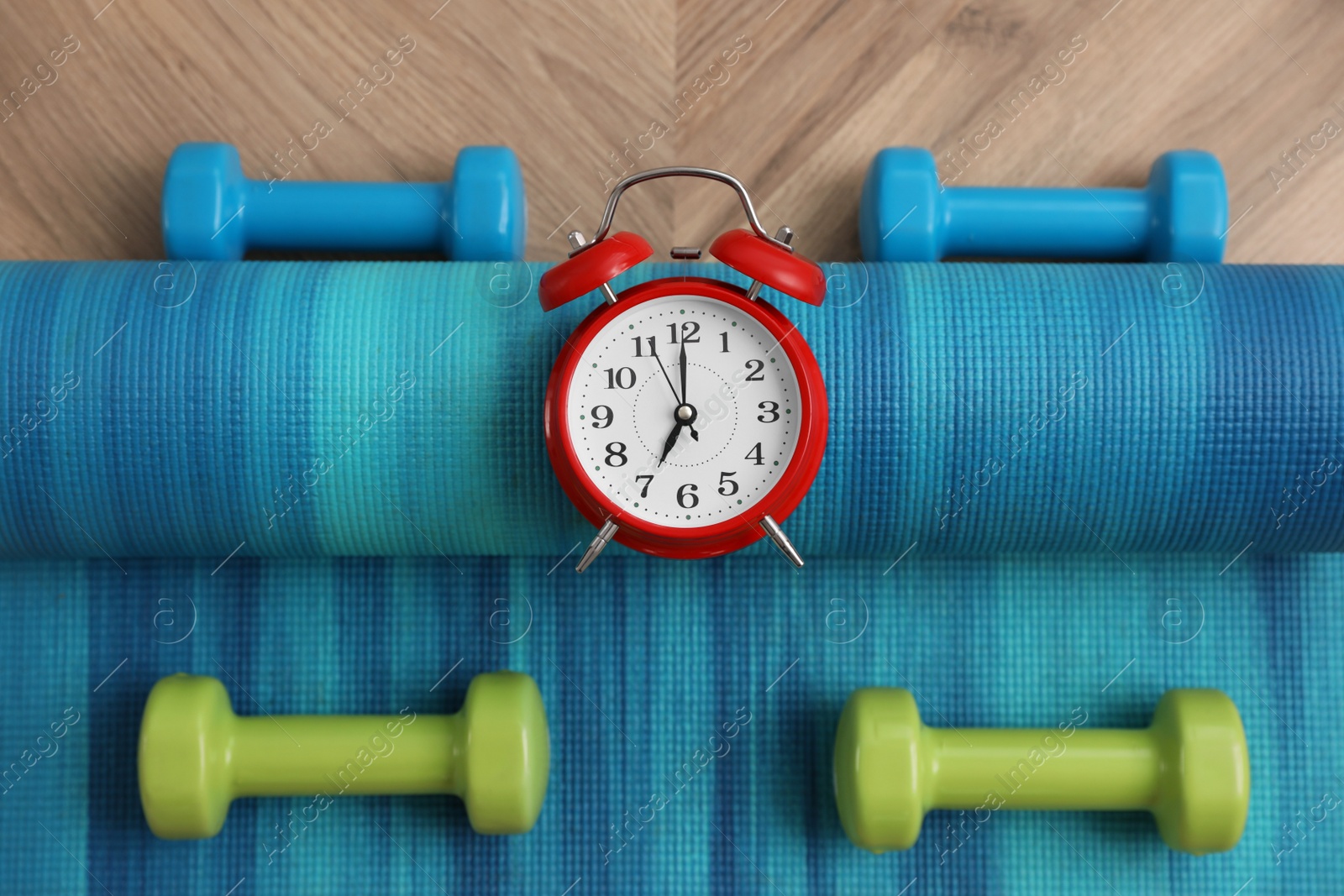 Photo of Alarm clock, yoga mat and dumbbells on wooden background, flat lay. Morning exercise