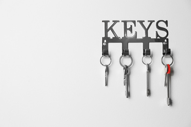 Photo of Metal key holder on light wall indoors. Space for text