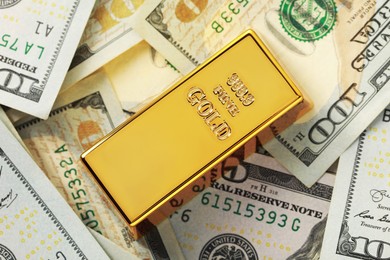 Shiny gold bar on dollar banknotes, top view