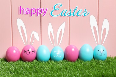 Image of Happy Easter. Several eggs with drawn faces and ears as bunnies among others on green grass against pink wooden background