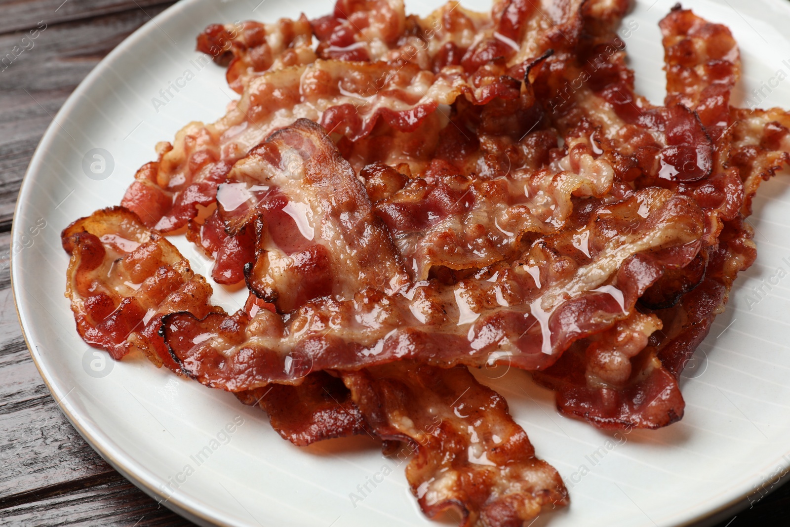 Photo of Slices of tasty fried bacon on wooden table, closeup