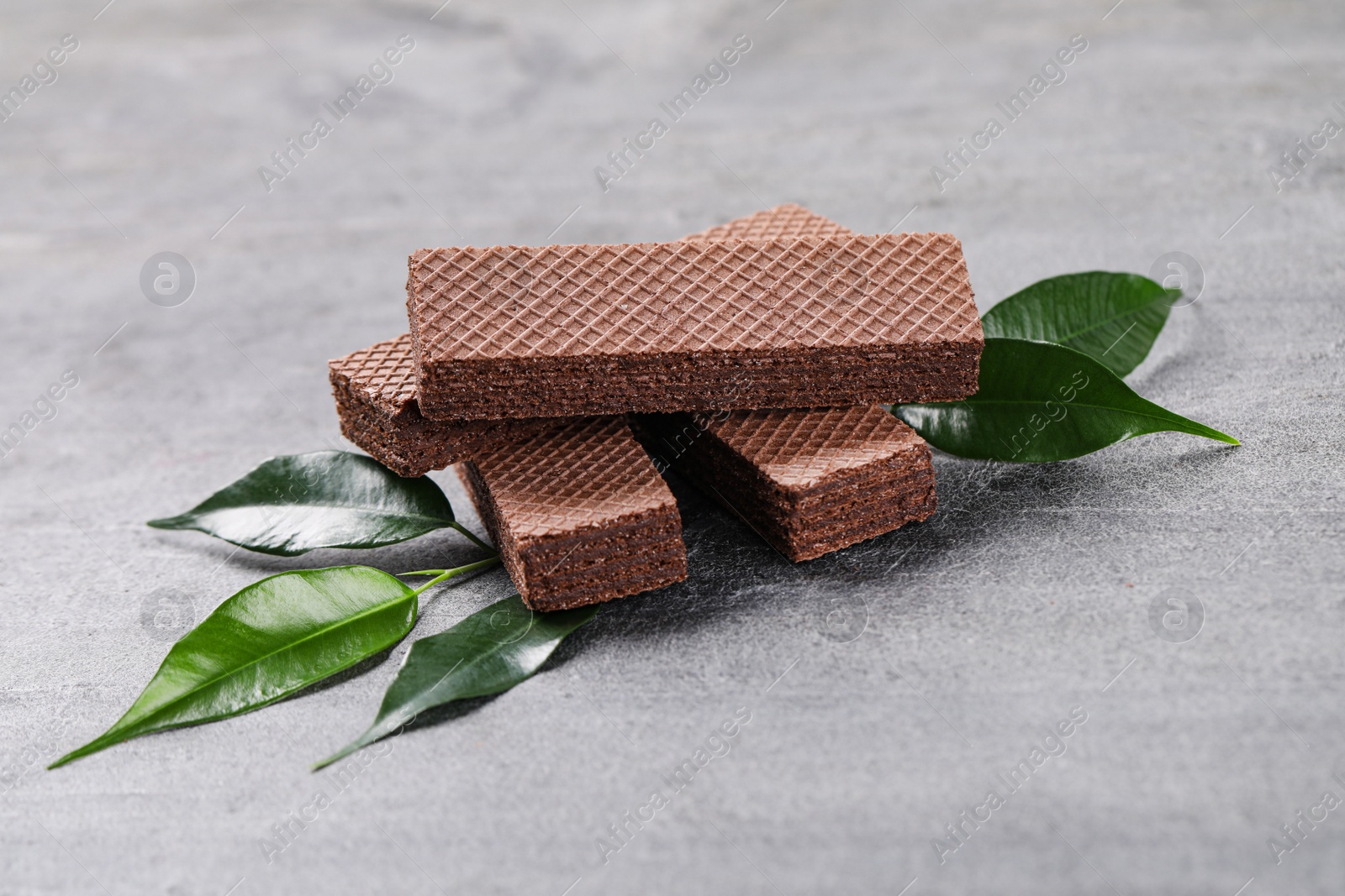 Photo of Delicious chocolate wafers with leaves on grey stone background