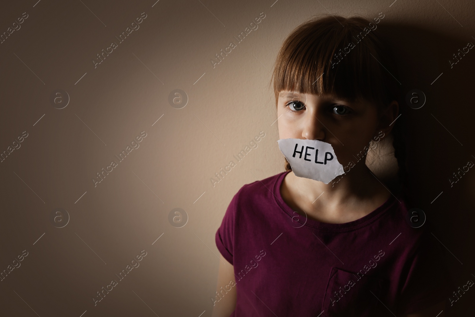 Photo of Sad little girl with sign HELP on beige background, space for text. Child in danger