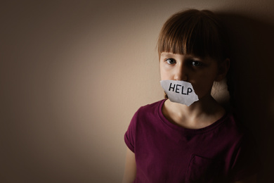 Sad little girl with sign HELP on beige background, space for text. Child in danger