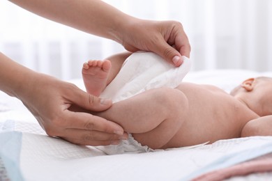 Mom changing baby's diaper on bed at home, closeup