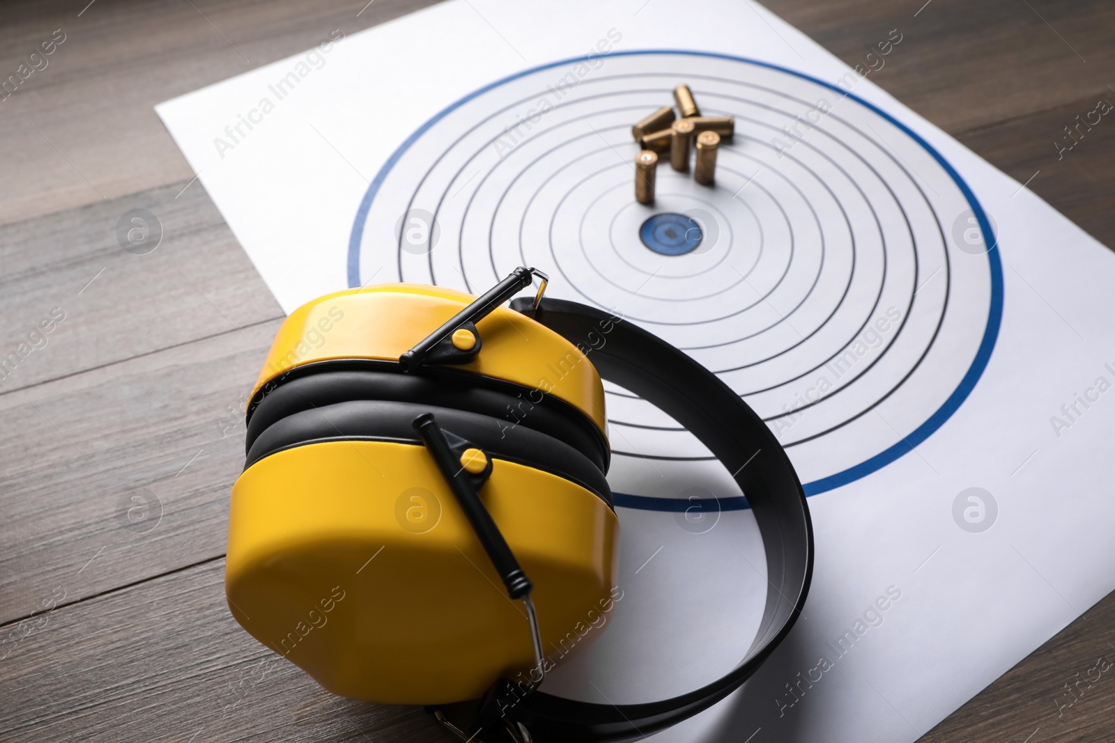 Photo of Shooting target, headphones and bullets on wooden table, closeup