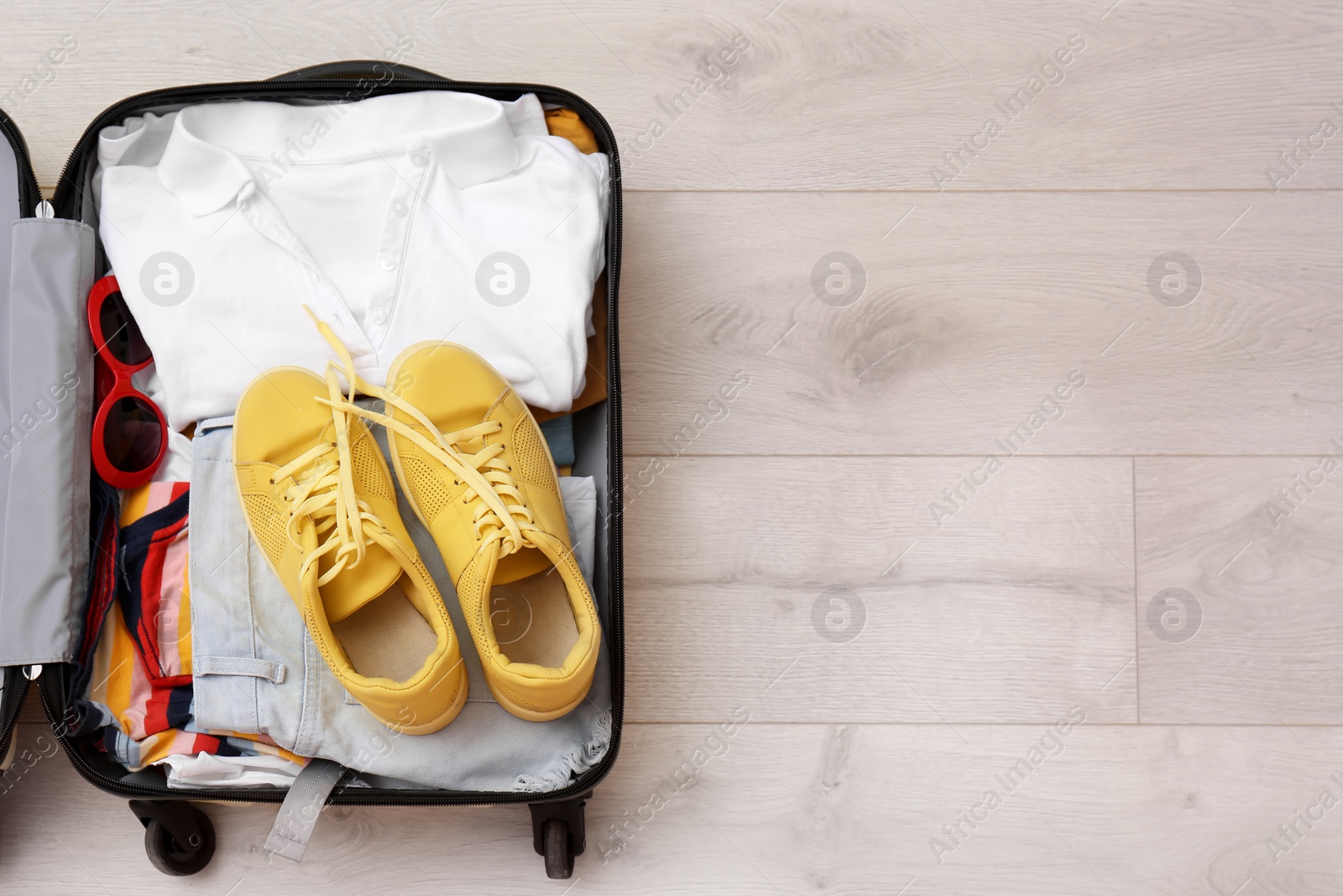 Photo of Packed suitcase with clothes and sneakers on wooden background, top view. Space for text