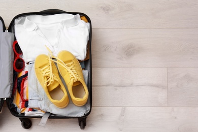 Packed suitcase with clothes and sneakers on wooden background, top view. Space for text