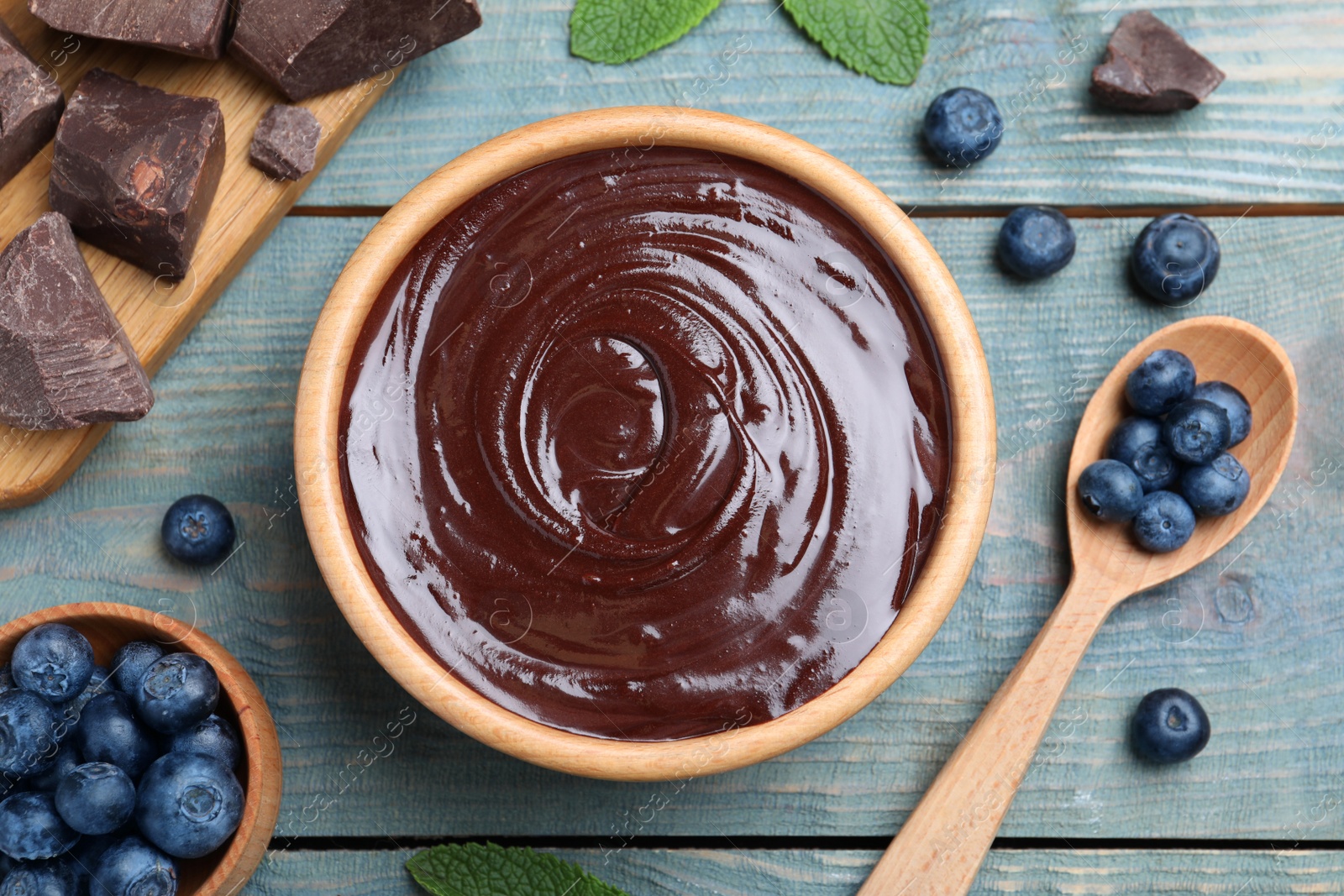 Photo of Delicious chocolate cream with blueberries and mint on light blue wooden table, flat lay