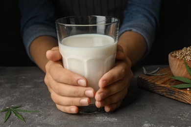 Photo of Woman with glass of hemp milk at grey table, closeup
