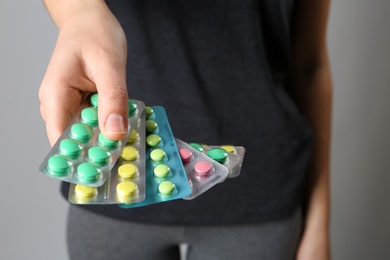 Photo of Woman holding pills in blister packs on gray background, closeup