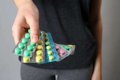 Woman holding pills in blister packs on gray background, closeup