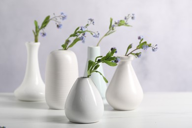 Photo of Beautiful forget-me-not flowers in vases on white marble table, closeup