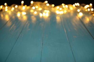 Photo of Blurred view of beautiful glowing lights, focus on light blue wooden table. Space for text