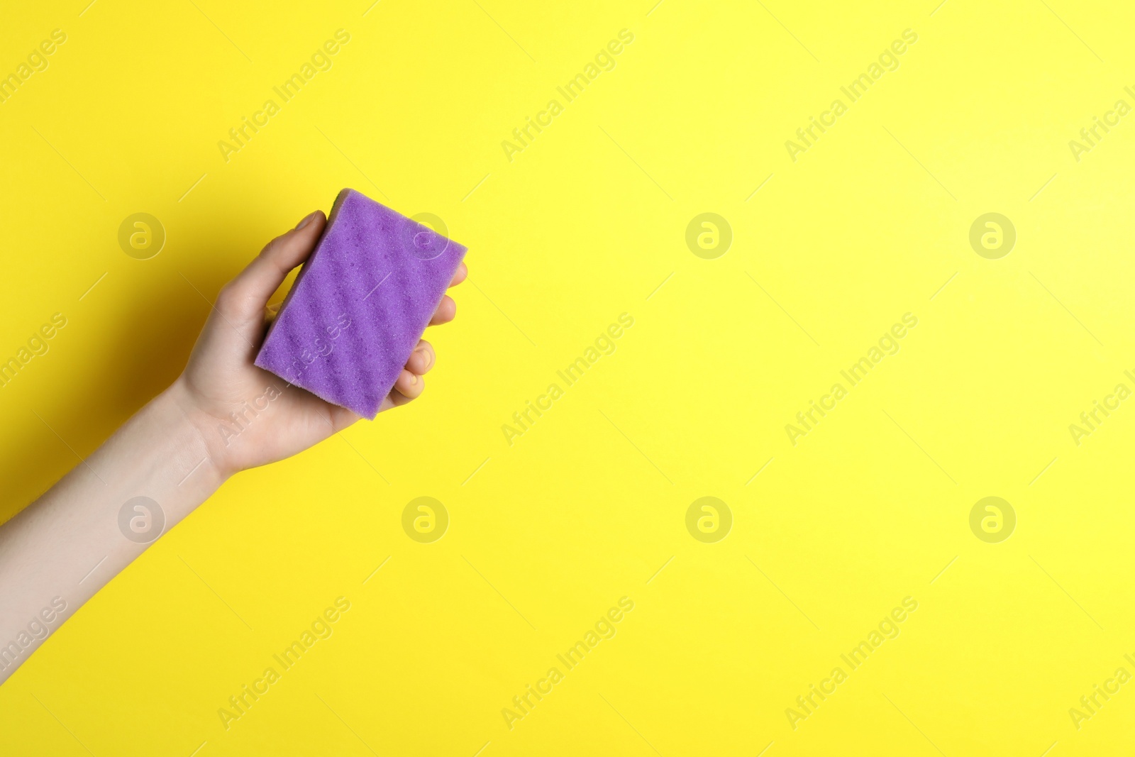 Photo of Woman holding sponge on yellow background, top view. Space for text