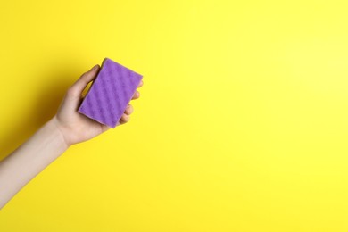 Woman holding sponge on yellow background, top view. Space for text