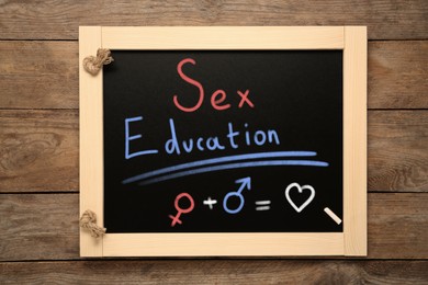 Image of Small black chalkboard with words Sex Education, heart, female and male gender signs on wooden background, top view