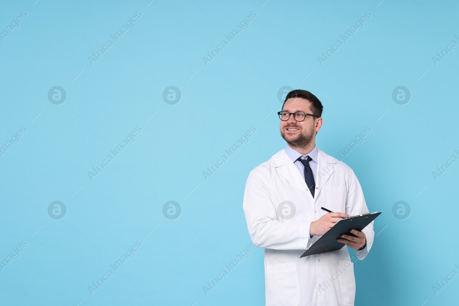 Photo of Smiling doctor with pen and clipboard on light blue background, space for text