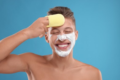 Photo of Happy young man washing off face mask with sponge on light blue background